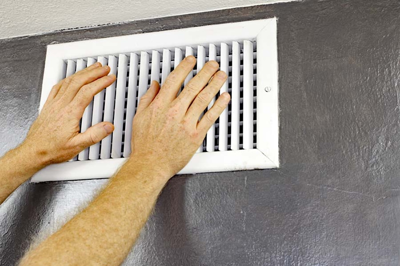 Two Hands in Front of an Air Vent Why Is My Air Conditioner Blowing Hot Air? A pair of adult male hands feeling the flow of air coming out of an air vent on a wall near a ceiling. Man with hands in front of an air vent feeling for air flow.